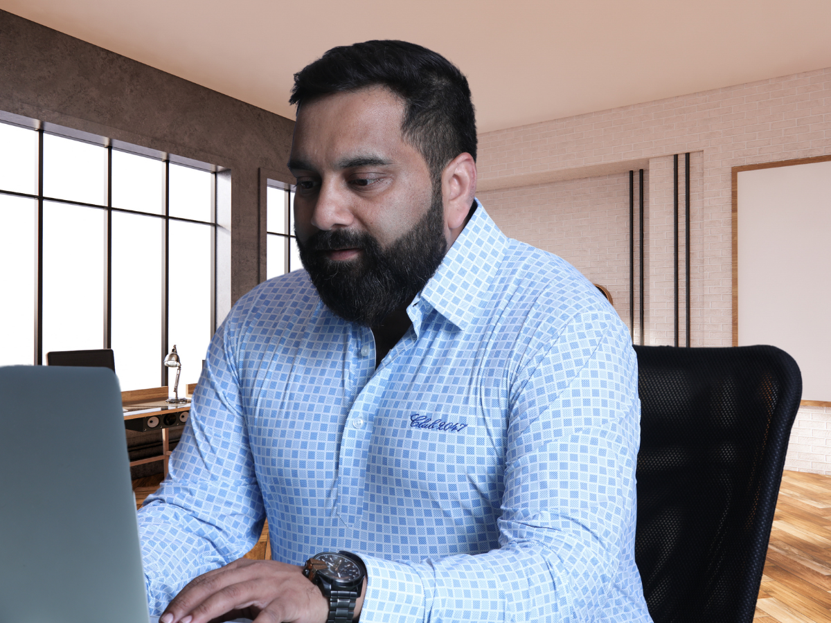 The Corporate Light Blue Checks Shirt worn while sitting in an office chair, showcasing its sleek light blue graphic checks design and comfortable, all-day fit ideal for business settings.